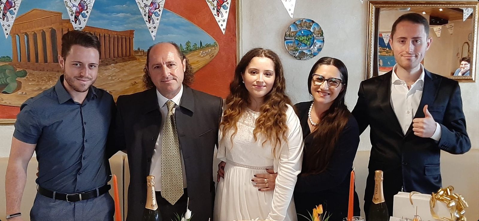 Fünf Mitglieder der Familie Borsellino stehen lächelnd nebeneinander im Restaurant, hinter ihnen ein Wandbild mit einem griechischen Tempel aus Sizilien
